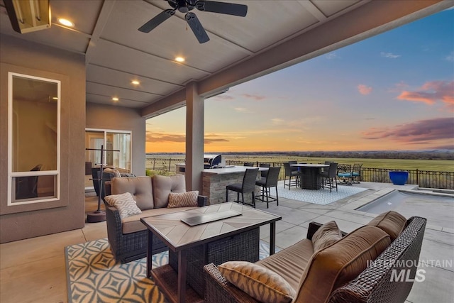 patio terrace at dusk featuring outdoor lounge area, outdoor dining area, fence, and ceiling fan