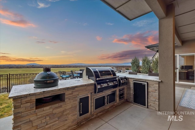 patio terrace at dusk featuring exterior kitchen, area for grilling, and fence