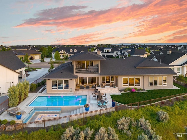 back of house featuring a patio, a fenced backyard, a residential view, a balcony, and an in ground hot tub