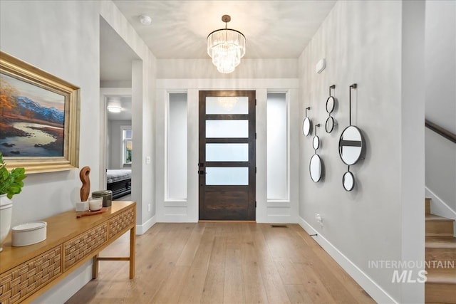 foyer entrance with stairway, a notable chandelier, baseboards, and light wood-type flooring