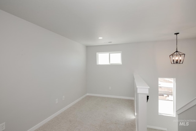 spare room featuring an inviting chandelier, carpet flooring, and baseboards