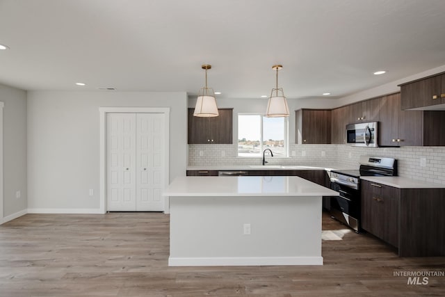 kitchen with dark brown cabinetry, modern cabinets, appliances with stainless steel finishes, decorative light fixtures, and light countertops