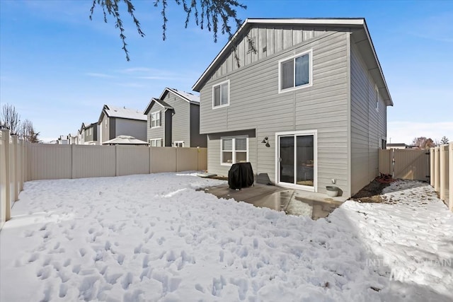 snow covered rear of property featuring board and batten siding and a fenced backyard