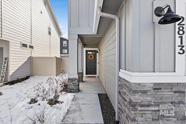 snow covered property entrance featuring board and batten siding and fence