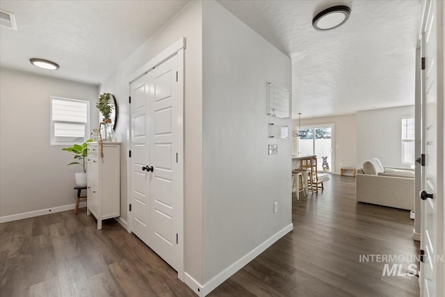 hall featuring a textured ceiling, baseboards, and wood finished floors