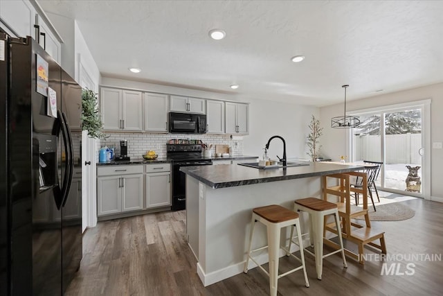 kitchen with dark countertops, backsplash, a sink, black appliances, and a kitchen bar