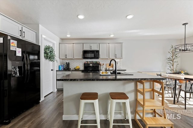 kitchen with black appliances, a kitchen bar, dark wood finished floors, and backsplash