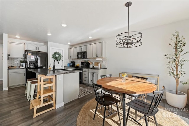 kitchen with dark wood finished floors, a center island with sink, dark countertops, a sink, and black appliances