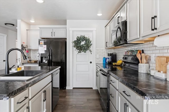 kitchen with black appliances, dark wood-style flooring, dark countertops, and a sink