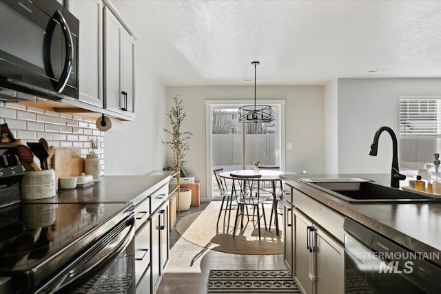 kitchen featuring decorative light fixtures, backsplash, a sink, wood finished floors, and black appliances