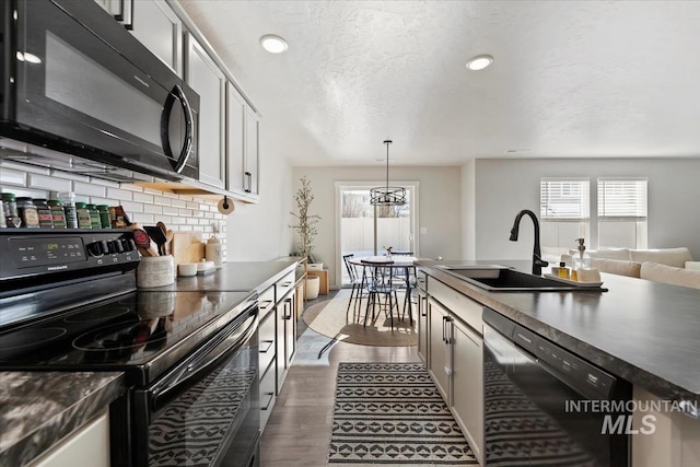 kitchen with dark countertops, black appliances, backsplash, and a sink