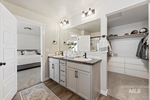 ensuite bathroom featuring double vanity, wood finished floors, and a sink