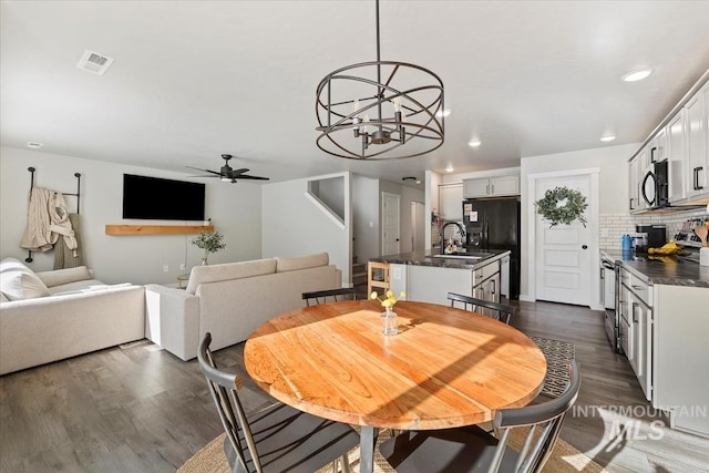 dining space with dark wood-type flooring, recessed lighting, visible vents, and ceiling fan with notable chandelier