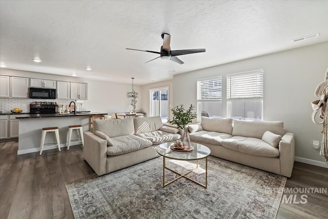 living area with ceiling fan, a textured ceiling, visible vents, baseboards, and dark wood-style floors