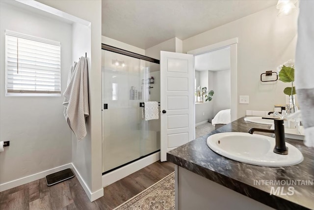 bathroom featuring double vanity, a stall shower, a sink, wood finished floors, and baseboards