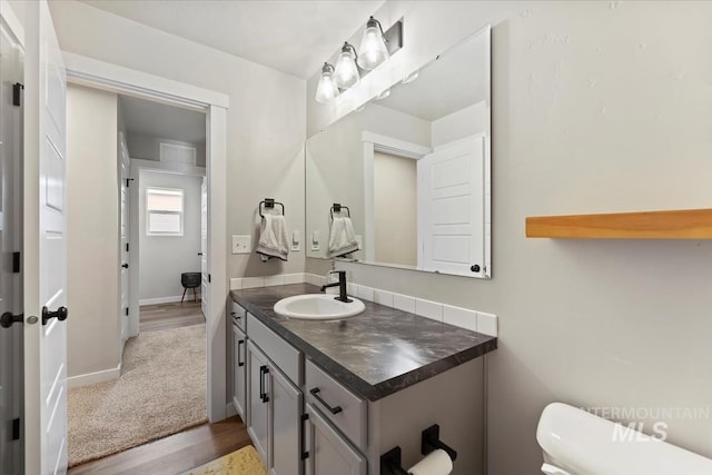 half bath with baseboards, vanity, toilet, and wood finished floors