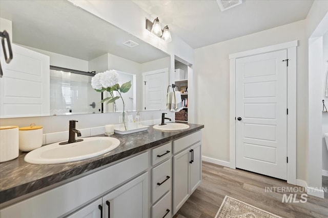 full bath with double vanity, visible vents, a sink, and wood finished floors