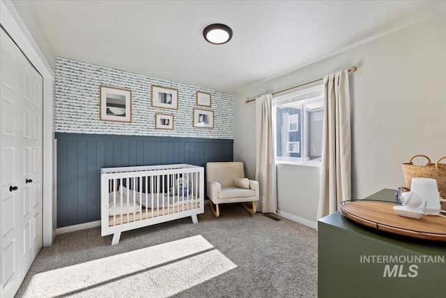 bedroom with a crib, wallpapered walls, wainscoting, carpet, and a closet