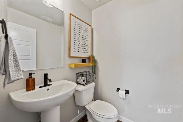 half bathroom with toilet, a sink, visible vents, and baseboards