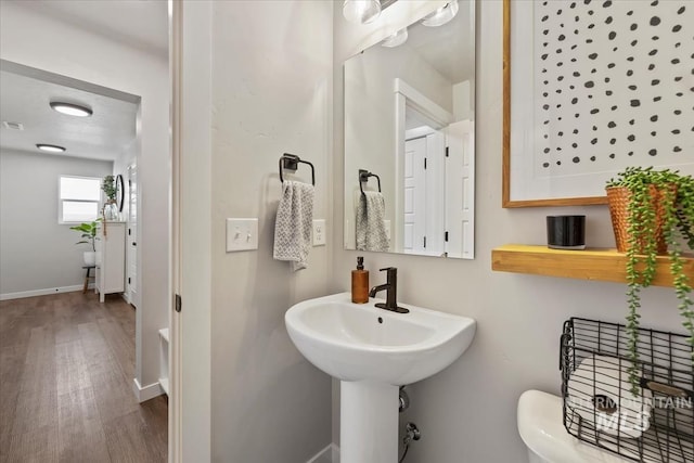 half bath featuring wood finished floors, visible vents, and baseboards