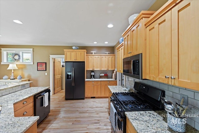kitchen with dishwasher, stainless steel gas range oven, light wood finished floors, backsplash, and black fridge