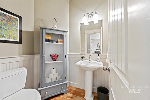 half bath featuring toilet, a sink, wood finished floors, and a wainscoted wall