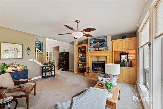 living area with light carpet, a fireplace, a ceiling fan, baseboards, and stairway
