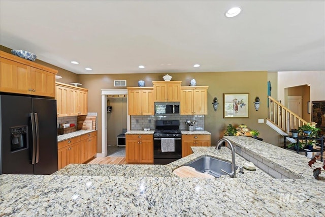 kitchen with a sink, light wood-style flooring, backsplash, and black appliances