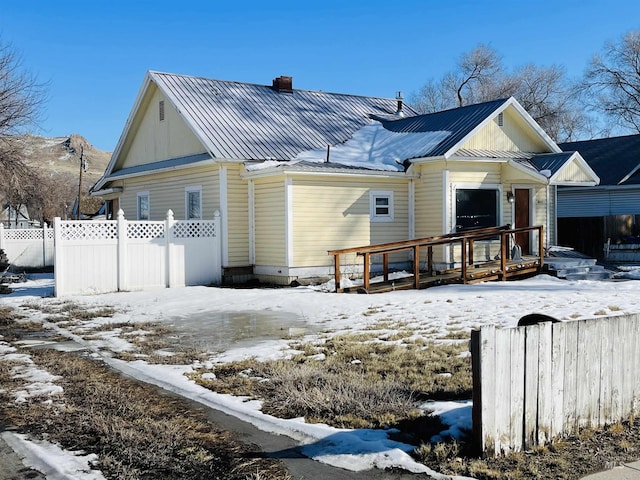 view of front of house with a chimney, metal roof, a standing seam roof, fence, and a wooden deck