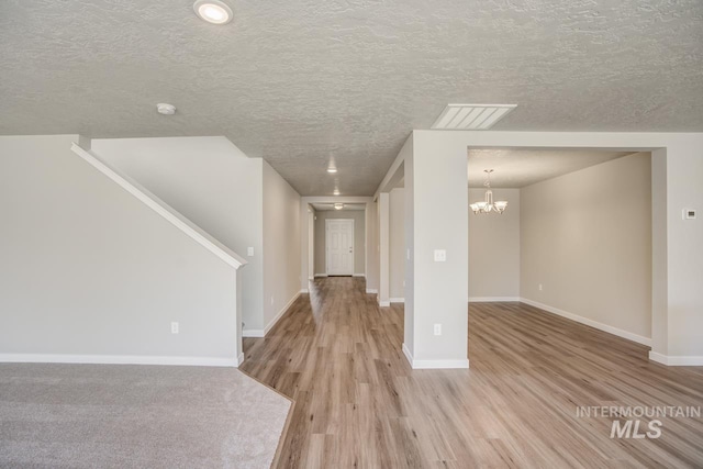 unfurnished living room featuring a textured ceiling, light hardwood / wood-style flooring, and a chandelier