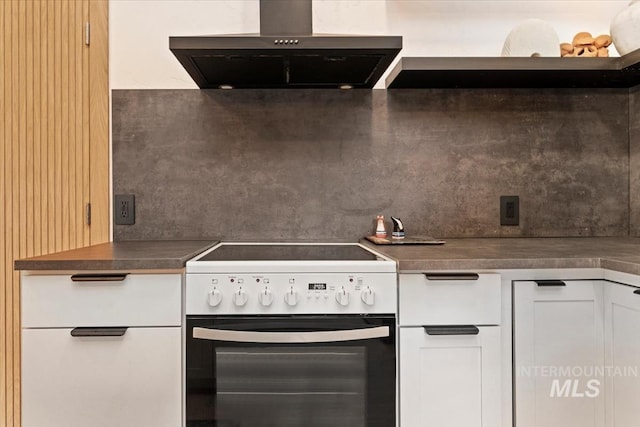 kitchen featuring wall chimney exhaust hood, dark countertops, tasteful backsplash, white cabinetry, and white range with electric cooktop