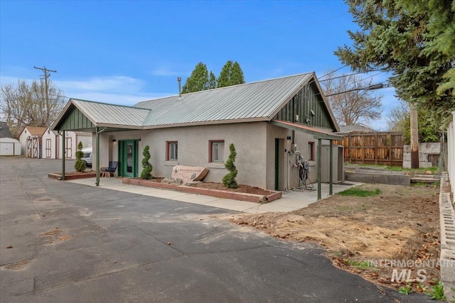 exterior space featuring an outbuilding, stucco siding, fence, metal roof, and a storage shed
