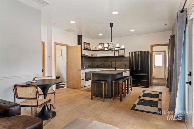 kitchen featuring freestanding refrigerator, a kitchen bar, a center island, light wood-style floors, and an inviting chandelier