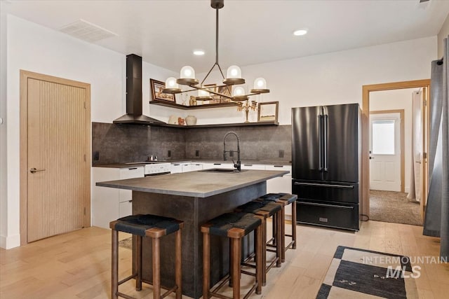 kitchen featuring a breakfast bar, a sink, light wood finished floors, wall chimney range hood, and high quality fridge