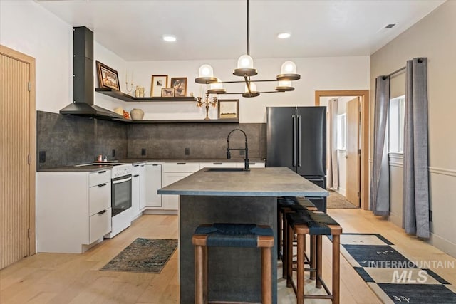 kitchen featuring a sink, wall chimney exhaust hood, high end black refrigerator, white range with electric stovetop, and white cabinets