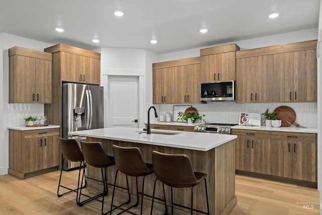 kitchen featuring light hardwood / wood-style floors, a kitchen bar, a kitchen island with sink, appliances with stainless steel finishes, and sink