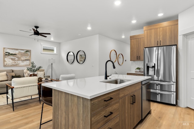 kitchen featuring stainless steel appliances, an island with sink, light wood-type flooring, ceiling fan, and sink