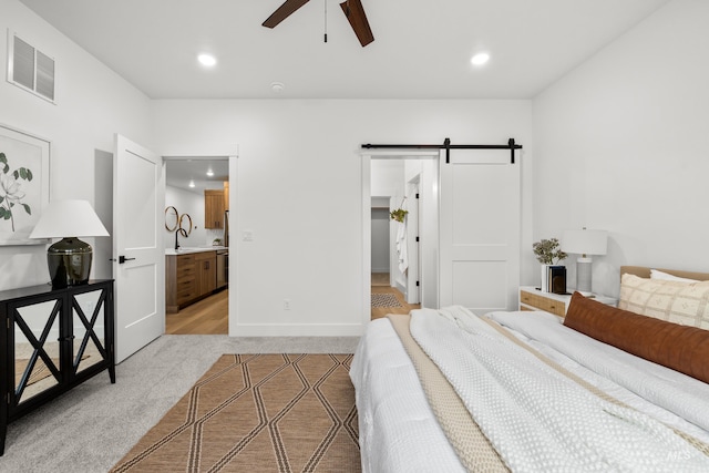 carpeted bedroom with ensuite bath, ceiling fan, and a barn door