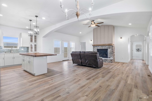kitchen with ceiling fan with notable chandelier, open floor plan, white cabinetry, a stone fireplace, and butcher block counters