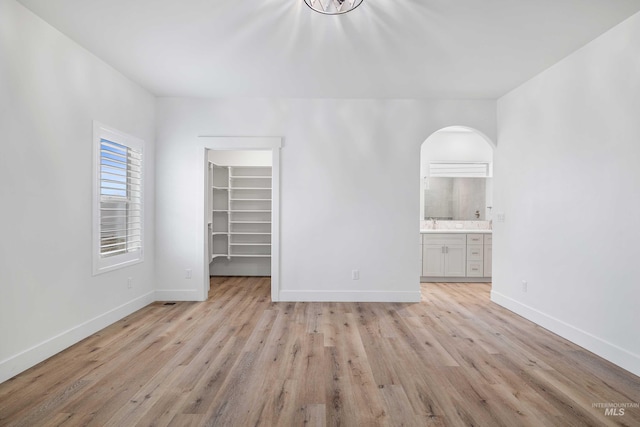 unfurnished bedroom featuring a spacious closet, light wood-style flooring, baseboards, and arched walkways