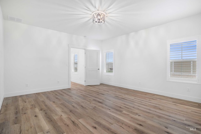 spare room with baseboards, an inviting chandelier, visible vents, and wood finished floors