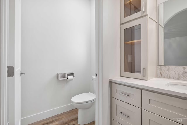 bathroom with toilet, wood finished floors, vanity, decorative backsplash, and baseboards