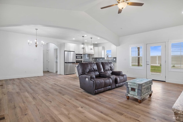 living room featuring vaulted ceiling, ceiling fan with notable chandelier, arched walkways, and light wood-style floors