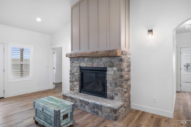 living area with a fireplace, light wood finished floors, baseboards, and arched walkways