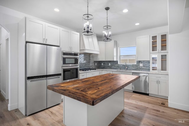 kitchen featuring butcher block counters, backsplash, a center island, white cabinets, and appliances with stainless steel finishes