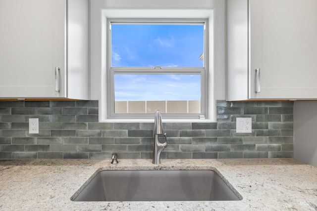 details featuring white cabinets, decorative backsplash, light stone countertops, and a sink