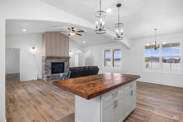 kitchen featuring lofted ceiling, a stone fireplace, butcher block counters, ceiling fan with notable chandelier, and open floor plan