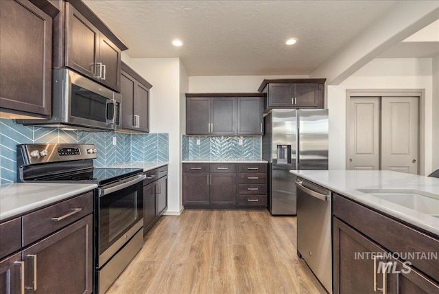 kitchen featuring stainless steel appliances, dark brown cabinets, light countertops, and light wood finished floors