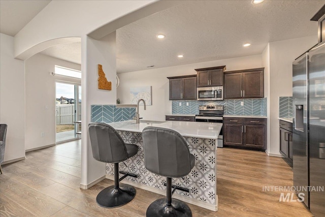 kitchen with arched walkways, light wood-style flooring, appliances with stainless steel finishes, and a sink