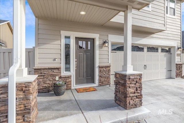 doorway to property featuring stone siding, covered porch, and concrete driveway